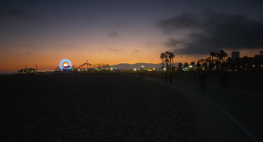 This 4K video shows the Santa Monica Pier in Los Angeles County, California. The visual documents the illuminated Pacific Wheel Ferris wheel and Pacific Park amusement structures. The composition illustrates the pier’s extension into the Pacific Ocean during twilight, documenting maritime urban engineering and Southern California coastal landmarks for editorial and travel media.