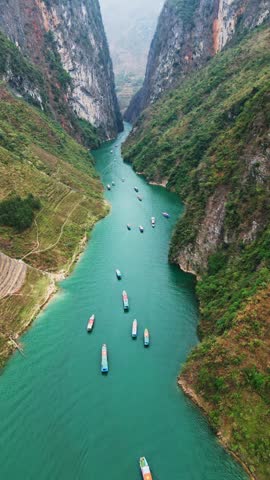 Vertical aerial view of a turquoise river flowing through a deep canyon with tourist boats navigating between steep cliffs in a dramatic mountain landscape in northern Vietnam