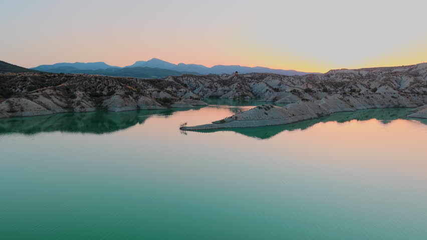 Aerial view of a reservoir landscape with dry hills and turquoise water at sunset