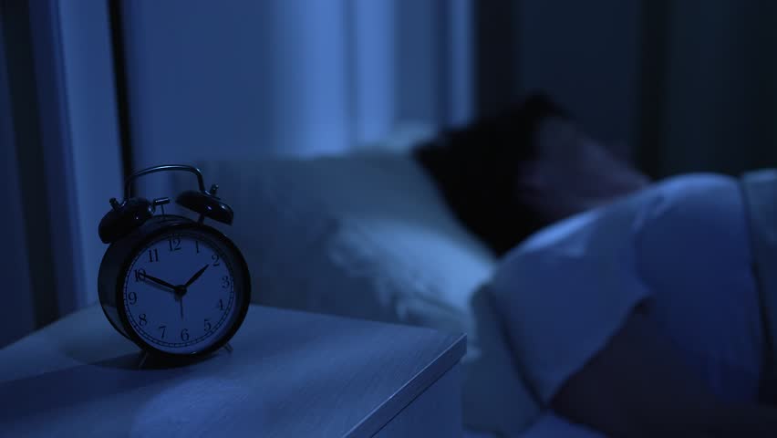 Elderly woman with insomnia tossing and turning looking at clock