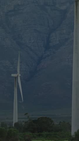 Vertical video: Neon lines emerging from left tracing turbine across mountain showing wind power. Towers, rotor, ridge, rockface, glow, fluorescent, vertical video