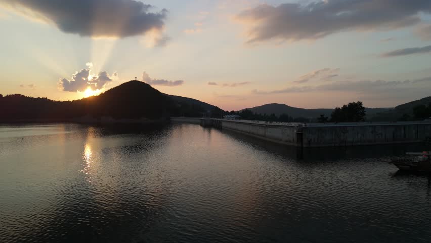 Sunset over calm lake with dramatic clouds and reflected sunlight. Scenic landscape view with peaceful evening atmosphere.