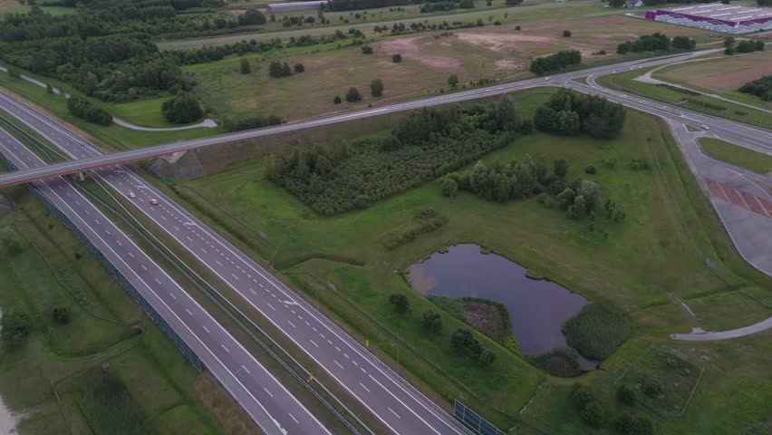 Aerial view of highway bridge crossing rural landscape with fields and roads. Drone shot showing transport infrastructure at dusk.