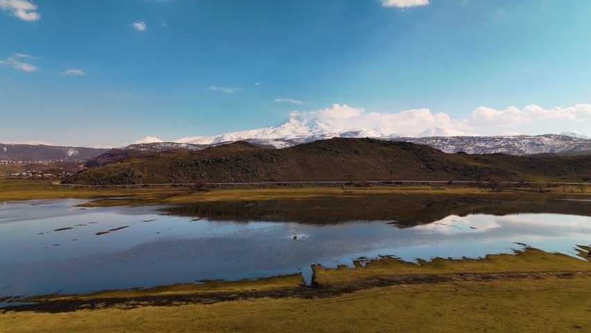 Stunning reflection of snowy mountains and clouds on a calm lake surface, aerial shot