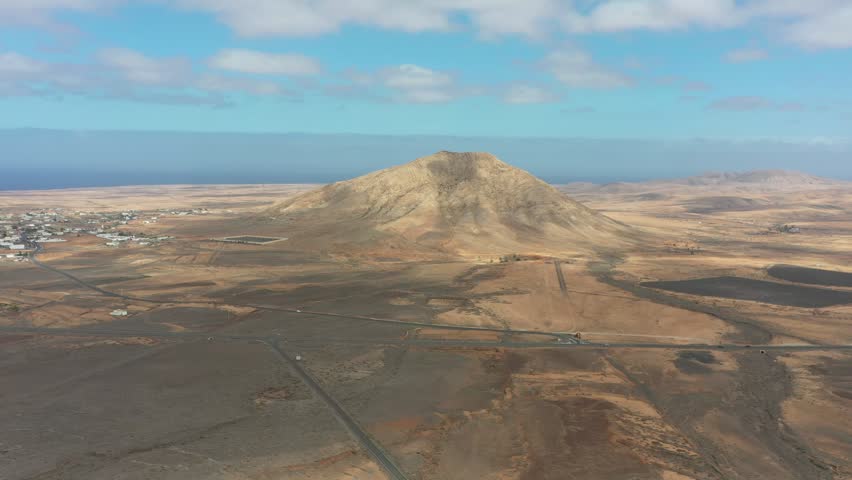 High-resolution drone footage of Tindaya Mountain standing isolated in the vast plains of Fuerteventura. The clip emphasizes the minimalistic beauty of the Canary Islands’ volcanic environment, with earthy tones, soft shadows, and a sense of untouched nature.