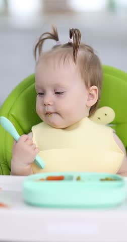 Cute little child eating baby food on feeding chair at home
