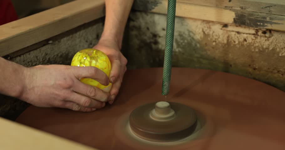 Worker polishing glass product on grinding wheel in factory, closeup