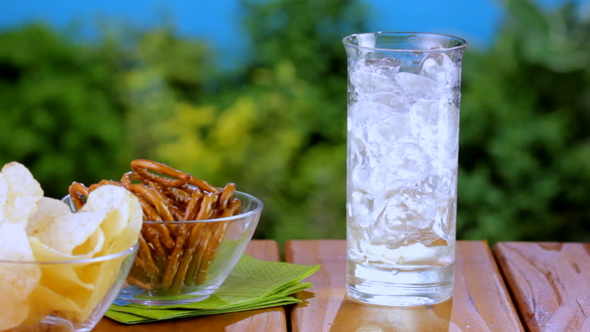 Ginger Ale is poured into glass on picnic table with pretzels and chips, shot in