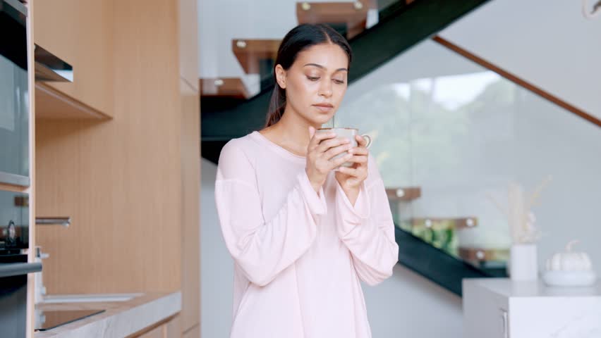 Beautiful Young Woman In Pink Pajamas Enjoying Hot Coffee In Modern Kitchen During Morning Routine. Relaxed Female Holding Cup With Tea And Thinking About New Day Plan Cozy Atmosphere At Home Or Hotel