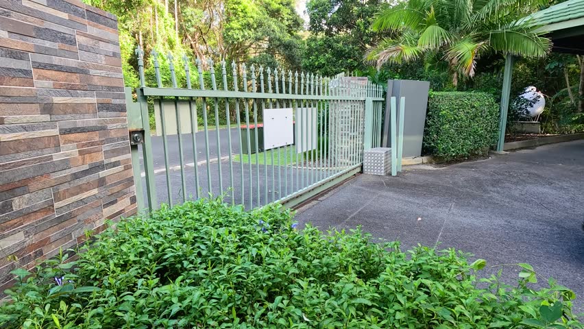 Sliding security gate opening, black vehicle arriving, modern home entrance.