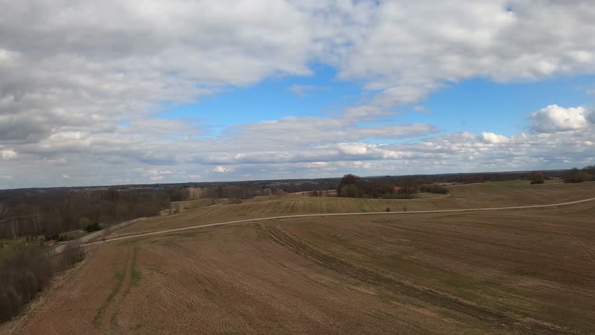 Wide countryside landscape with lake, trees, and a house under a dramatic cloudy sky.