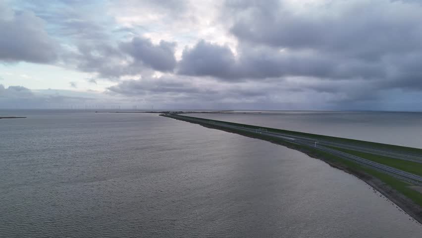 High aerial view of the Afsluitdijk approach at dusk with cloudy sky and the first dam structures visible.