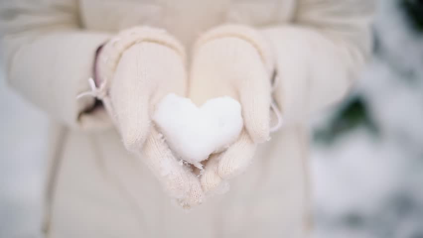 Woman hands holding heart made of snow in winter park close up shot of female palms in white mittens.