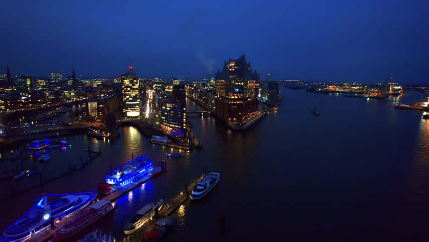 Aerial motion over Hamburg harbor during blue hour, featuring elbe philharmonic hall and city lights.