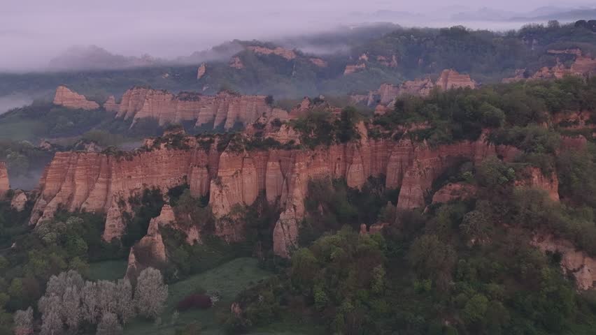 Aerial view of the unique Le Balze rock formations surrounded by lush greenery and morning mist in Reggello, Tuscany, Italy.