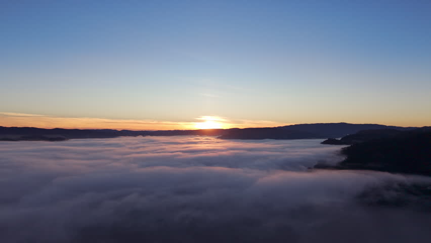 Sunrise above a calm sea of fog with distant hills and a soft gradient sky. Minimalistic aerial scene with smooth clouds in northern Europe.