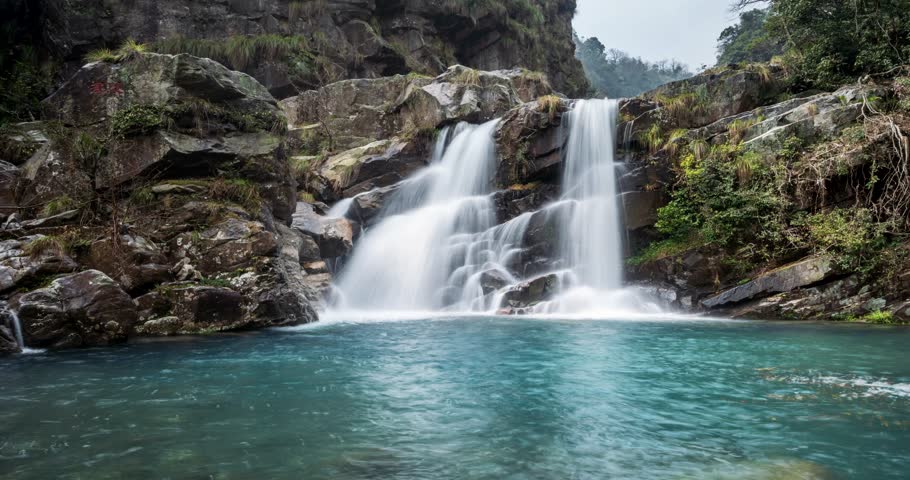 Time-lapse of the silky twin waterfalls cascade through a lush valley, with emerald pools and rocks under soft spring light, Lushan mountain, Jiangxi Province, China.