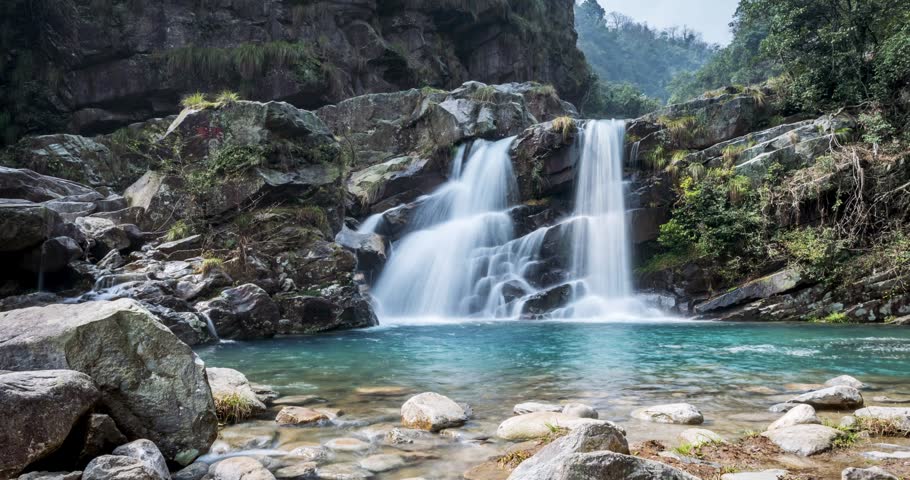 Time-lapse of the silky twin waterfalls cascade through a lush valley, captured via slider with ND filter for silky water and dynamic retreat perspective.