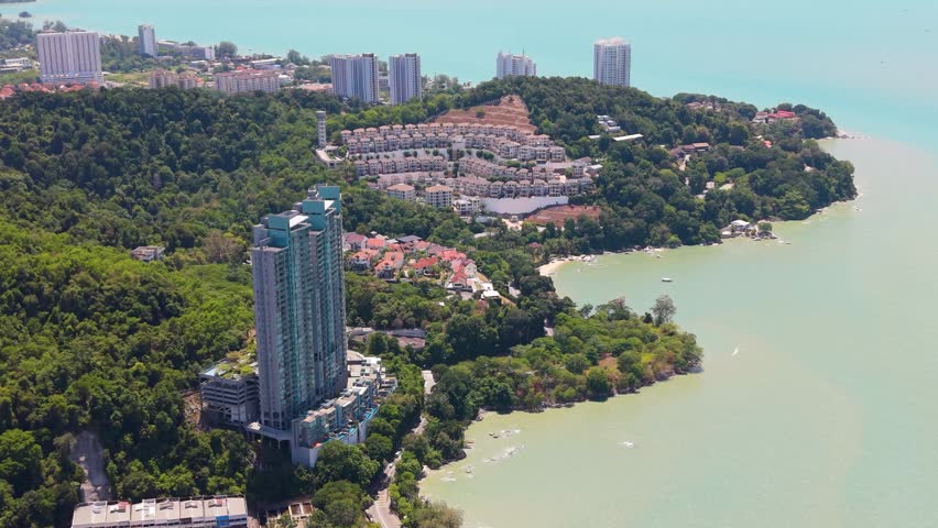 Aerial drone view of Batu Ferringhi on Penang Island, Malaysia, showing coastal skyline, beachfront resorts, lush greenery, and tropical shoreline landscape. UHD.