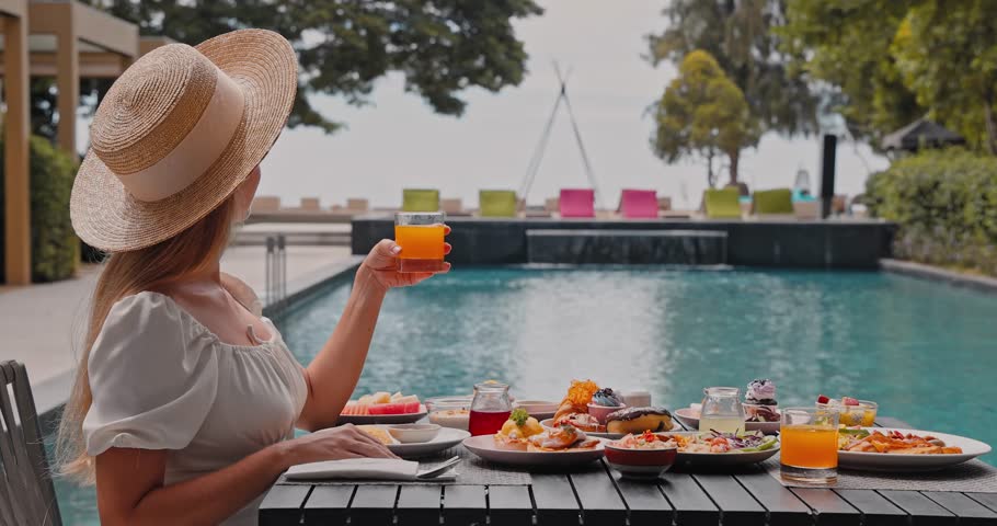 Young woman wearing straw hat drinking orange juice, luxury outdoor breakfast spread at tropical resort poolside, summer vacation lifestyle and high-end travel advertisement