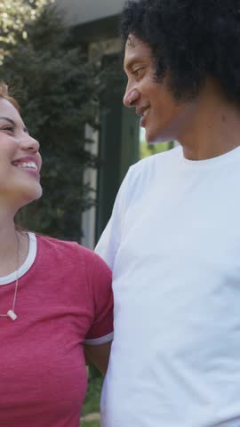 Vertical video: Sharing joke, couple laughing and leaning on porch, red and white shirts visible. Pair, outdoor, frontyard, closeup, candid, joy, vertical video