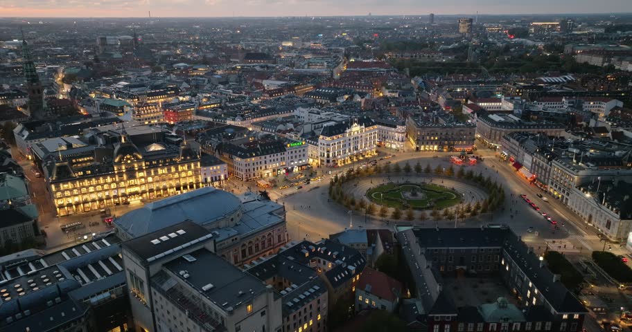 Aerial drone footage of Copenhagen city square at dusk with glowing lights and traffic motion.