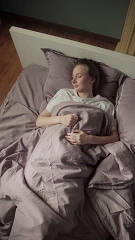 Young woman lying in bed, turning and tossing restlessly, unable to fall asleep due to anxiety, stress, insomnia, or a nightmare. Top down view of her troubled sleep in the bedroom