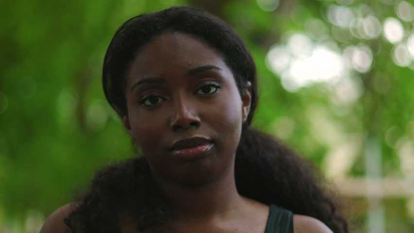 Woman maintaining soft eye contact and smiling gently suggesting positivity, approachability and relaxed confidence during peaceful time in park setting