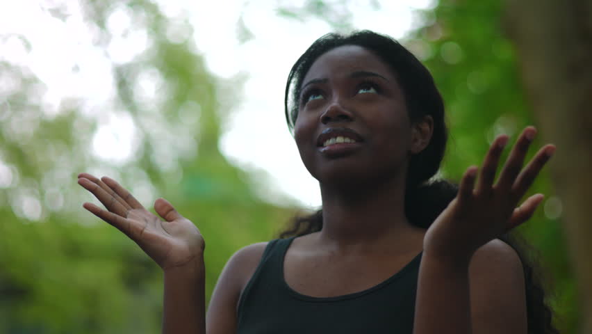 Woman transitioning from open gesture to quiet reflection suggesting gratitude, trust and inner peace during serene time in green park setting
