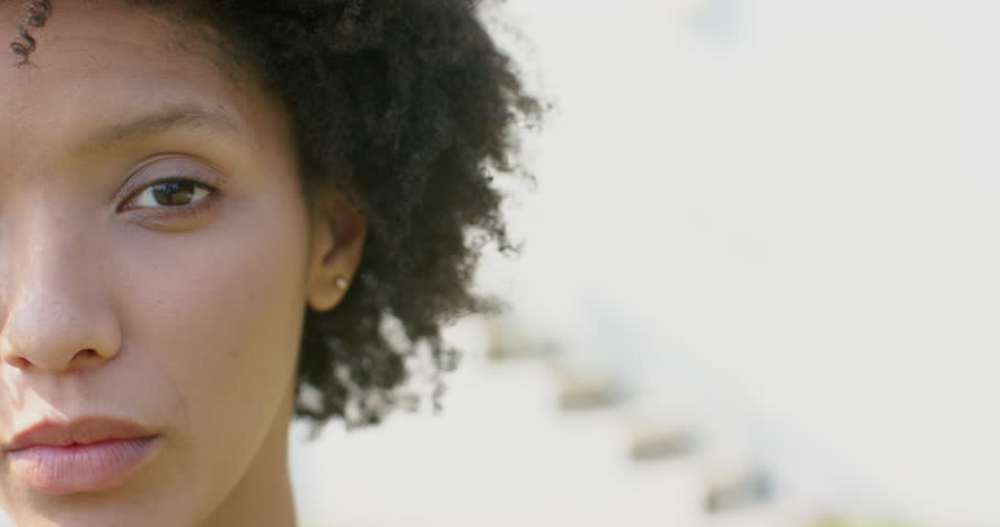woman blinking, shifting gaze in sunlight against wall with stud earring, blurred steps, copy space. Close-up, portrait, natural, outdoor, sunlight, minimalist, subtle