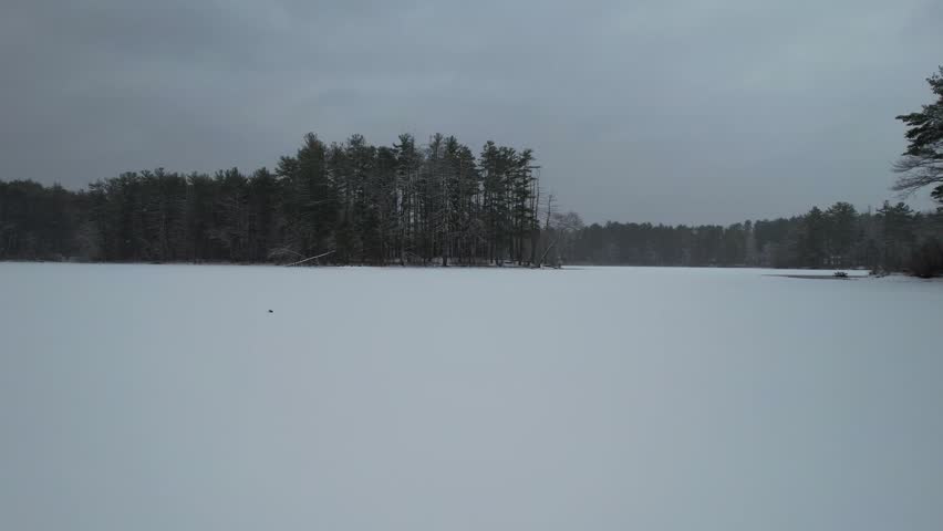 Fast aerial over frozen lake and snow covered landscape, Harold Parker State Forest, Massachusetts, USA