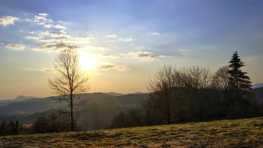 Time lapse of golden sunset over mountain ridge with trees in foreground