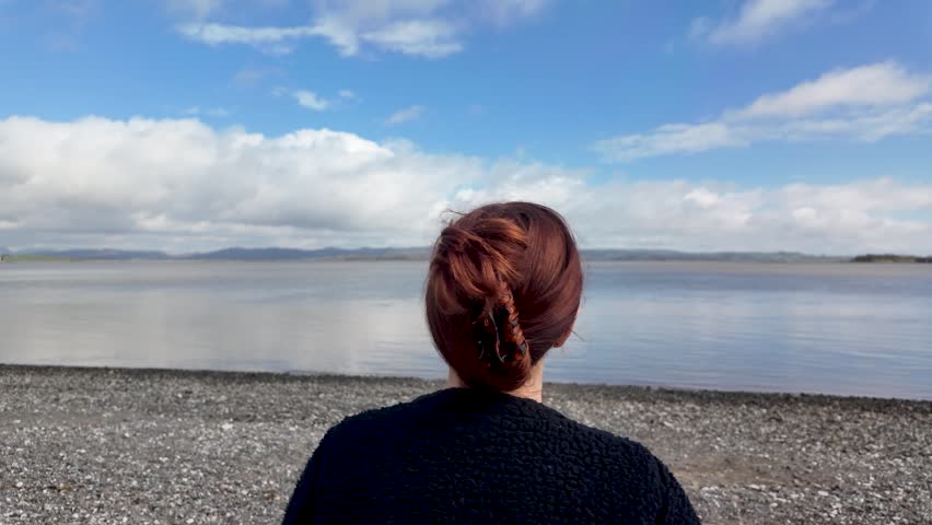 Woman looking out to sea, back view, feeling reflective
