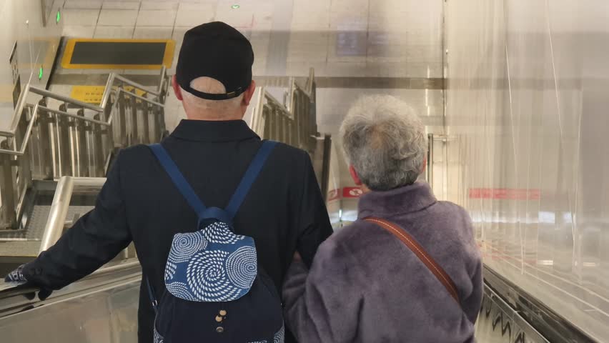 Elderly Woman and Companion Using Escalator in Subway Station, Beijing, China.