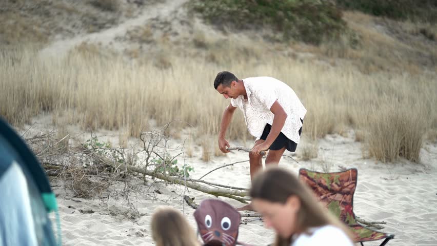 Mother prepares food and drinks at a beach campsite, focusing on a cooler filled with supplies. The scene captures a peaceful family moment, highlighting summer leisure and coastal adventure