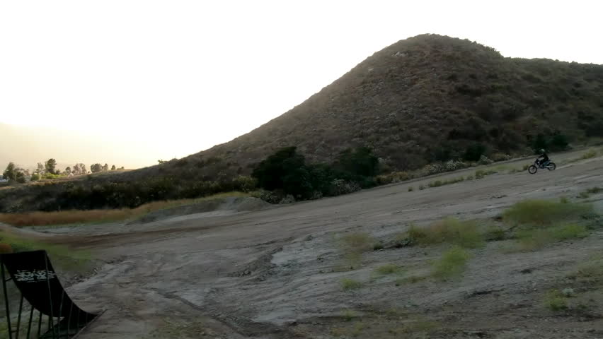 Motocross rider jumping off a dirt ramp and flying through the air during a scenic sunset