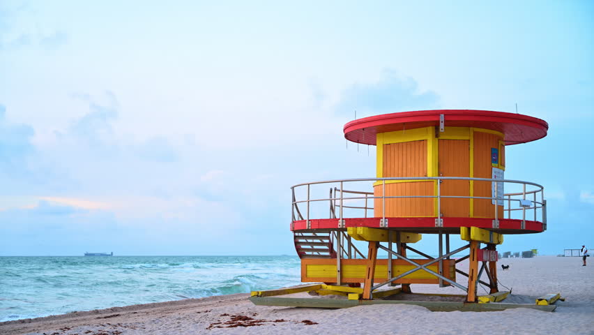 Iconic yellow and orange lifeguard tower on South Beach. Traditional colorful wooden lifeguard station on the sandy shore of Miami Beach under an overcast sky.