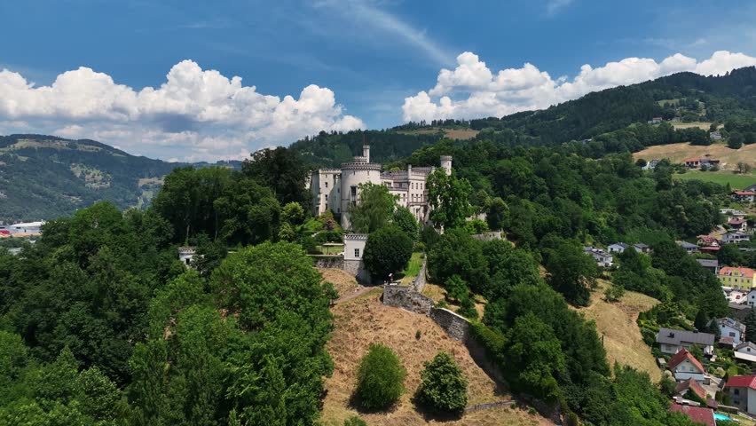 Aerial summer footage of Wolfsberg showing town center, church towers, green hills, layered valleys, warm light, smooth drone flight, atmospheric European small-town scenery
