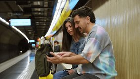 Happy young couple looking at a mobile phone together while sitting on a bench in an underground subway station, waiting for the train - Powered by Shutterstock - Get 15% off with code: PIKWIZARD15