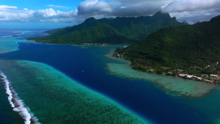 Opunohu Bay in Moorea, French Polynesia, aerial drone panorama landscape of with coral reef shallows, deep blue lagoon water, and jagged volcanic peaks under blue sky and clouds power boat in channel