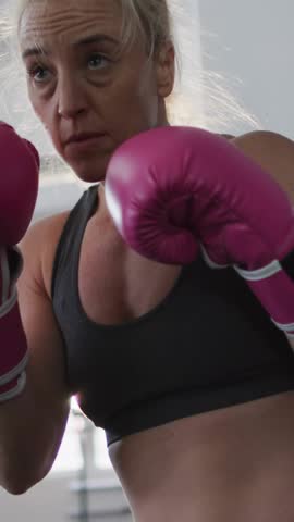 Vertical video: Woman punching toward camera with pink gloves, boxing HUD bars visualizing metrics. Athlete, fitness, training, cardio, studio, overlay, vertical video