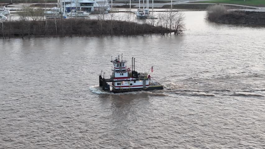 Aerial view of a boat navigating the murky river waters with a marina filled with boats docked in the background, Cincinnati, Ohio, United States.
