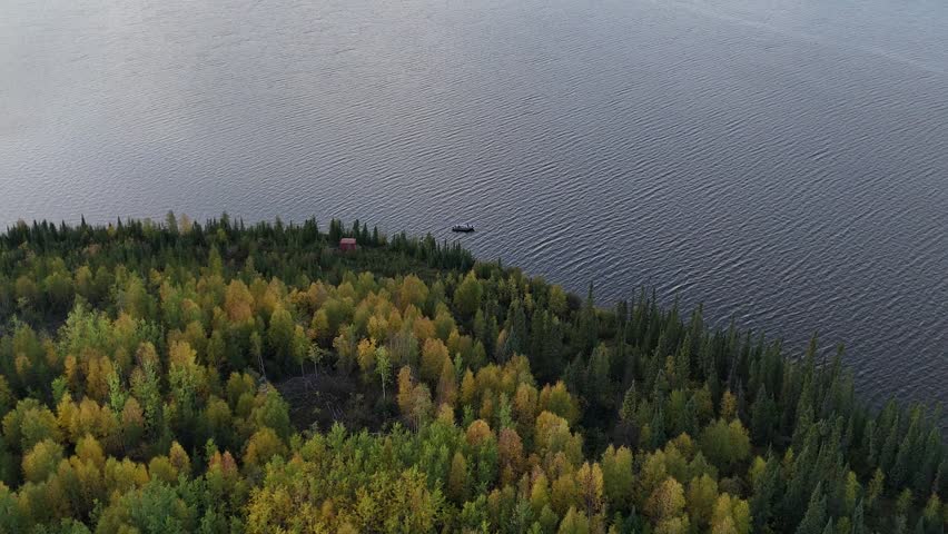 Aerial drone descends and moves toward a small fishing boat on a lake in northern Manitoba, Canada. Boreal forest with fall colors surrounds calm water in natural light.