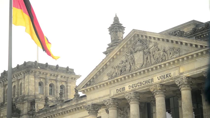 German flag waving near the Reichstag building under a cloudy sky, showcasing national identity and historic government architecture in Berlin.