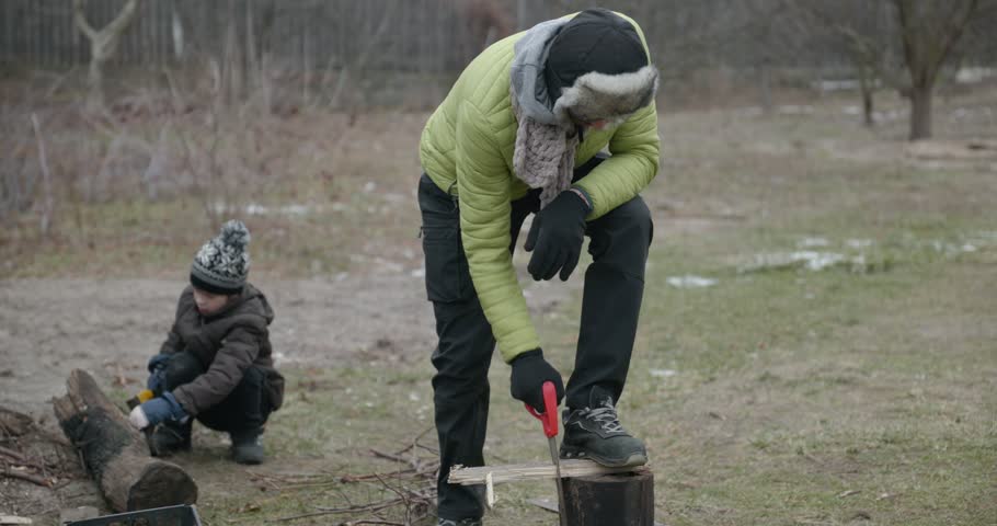 Men with kid cut branches in backyard and stockpile firewood in shed for winter. 4K 10-bit