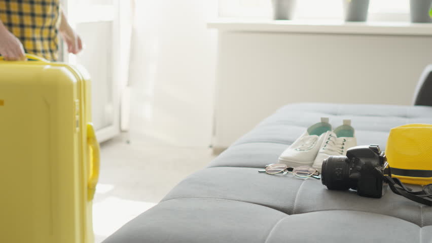A traveler prepares for their vacation with a vibrant yellow suitcase, a camera for memories, a stylish hat, and toiletries on a cozy sofa, all highlighting the excitement of travel