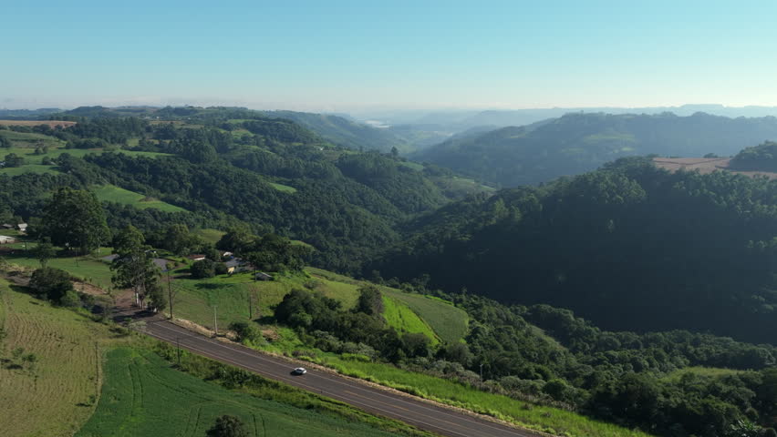 Rural valley aerial view showing farmland, native forest, rolling hills and country road.