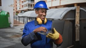 Man construction worker in blue hardhat and earmuffs holds laptop and types with gloved hand on building site; productivity focus. - Powered by Shutterstock - Get 15% off with code: PIKWIZARD15