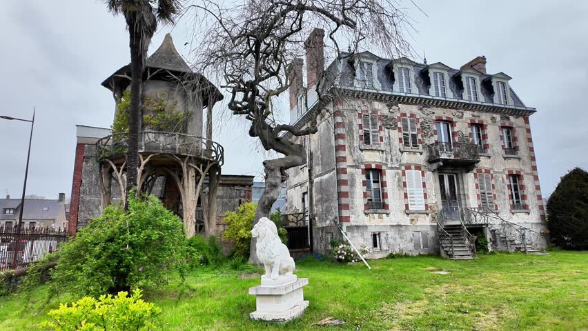 Panning shot of a grand historic French mansion with stone lion statues and a rustic wooden gazebo in the garden.