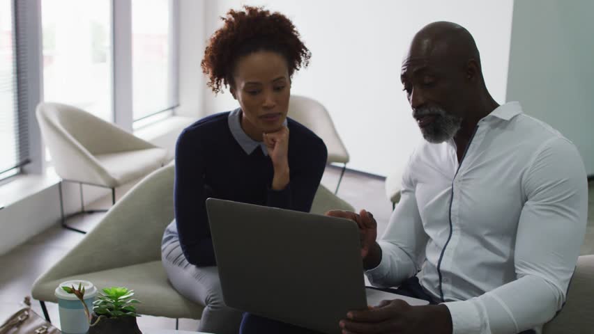 Man and woman sitting sofa, man angling laptop animating augmented business charts, discussing. Collaboration, analytics, data, graphs, infographics, overlay, office